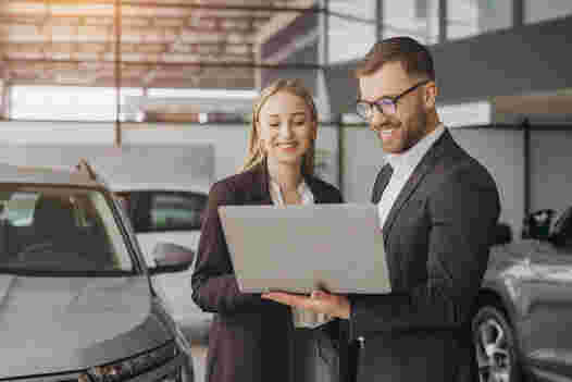 Two workers looking at a laptop in a car dealership