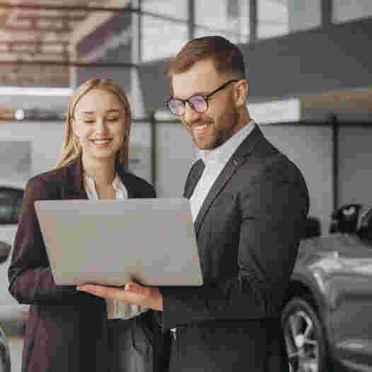 Two people within a car dealership looking at a laptop